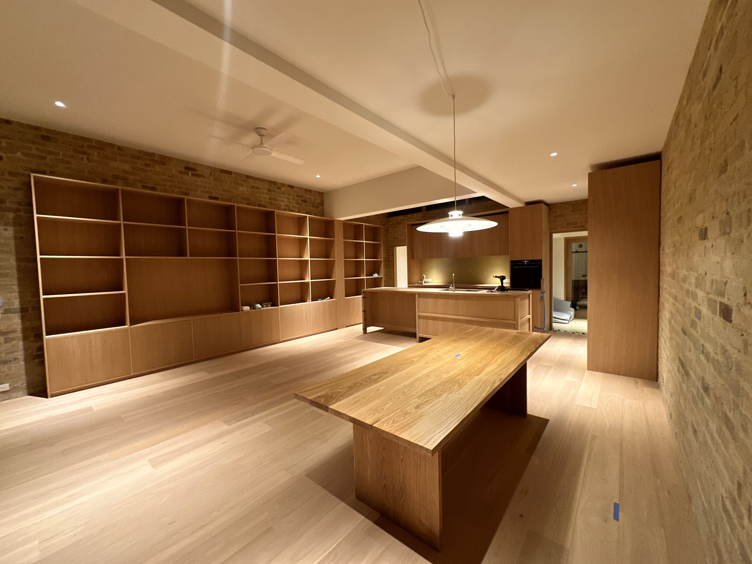 Empty timber shelving spanning a brick wall beside a kitchen island