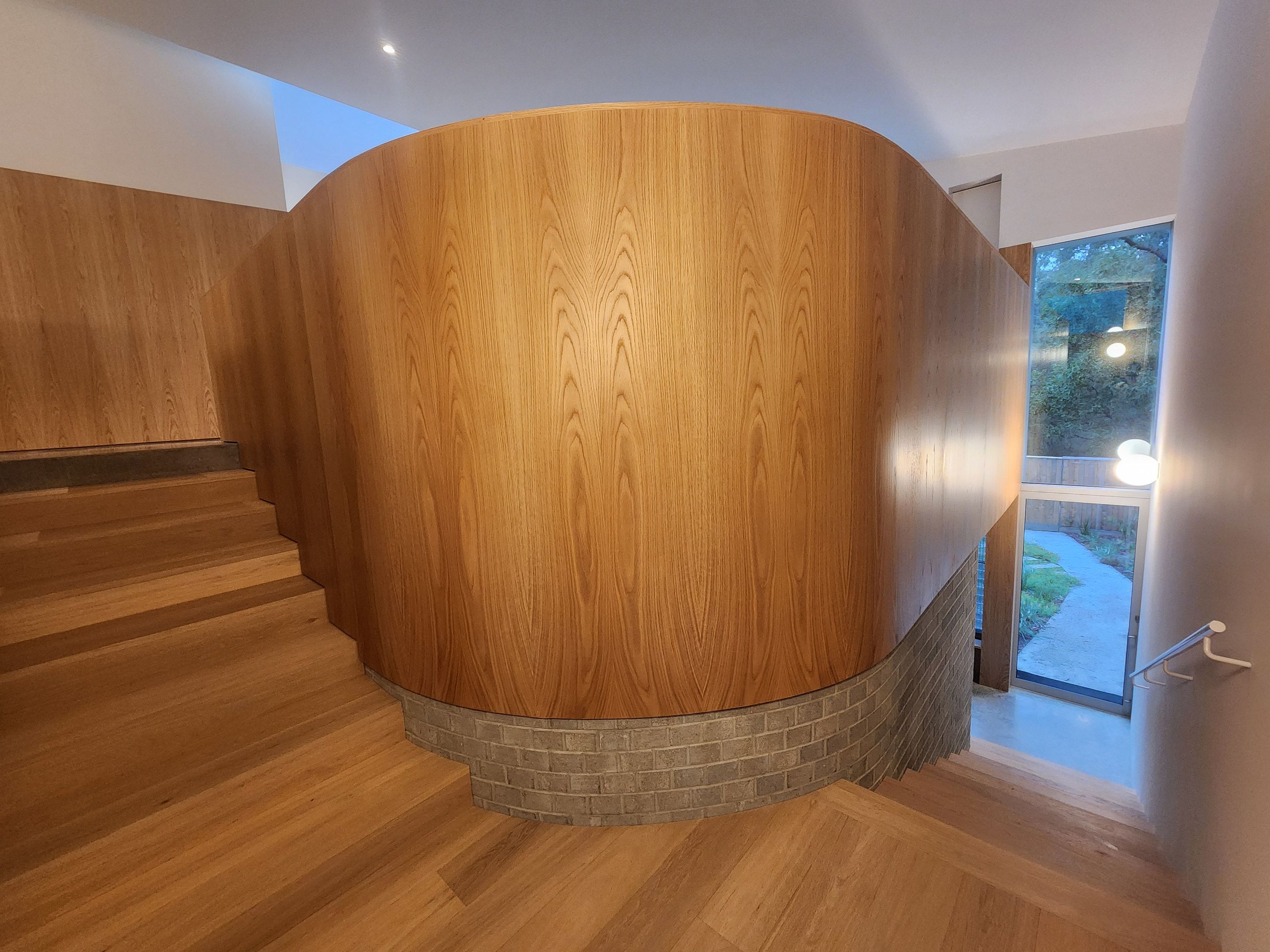 Curved timber-lined stair void beside a brick-based landing