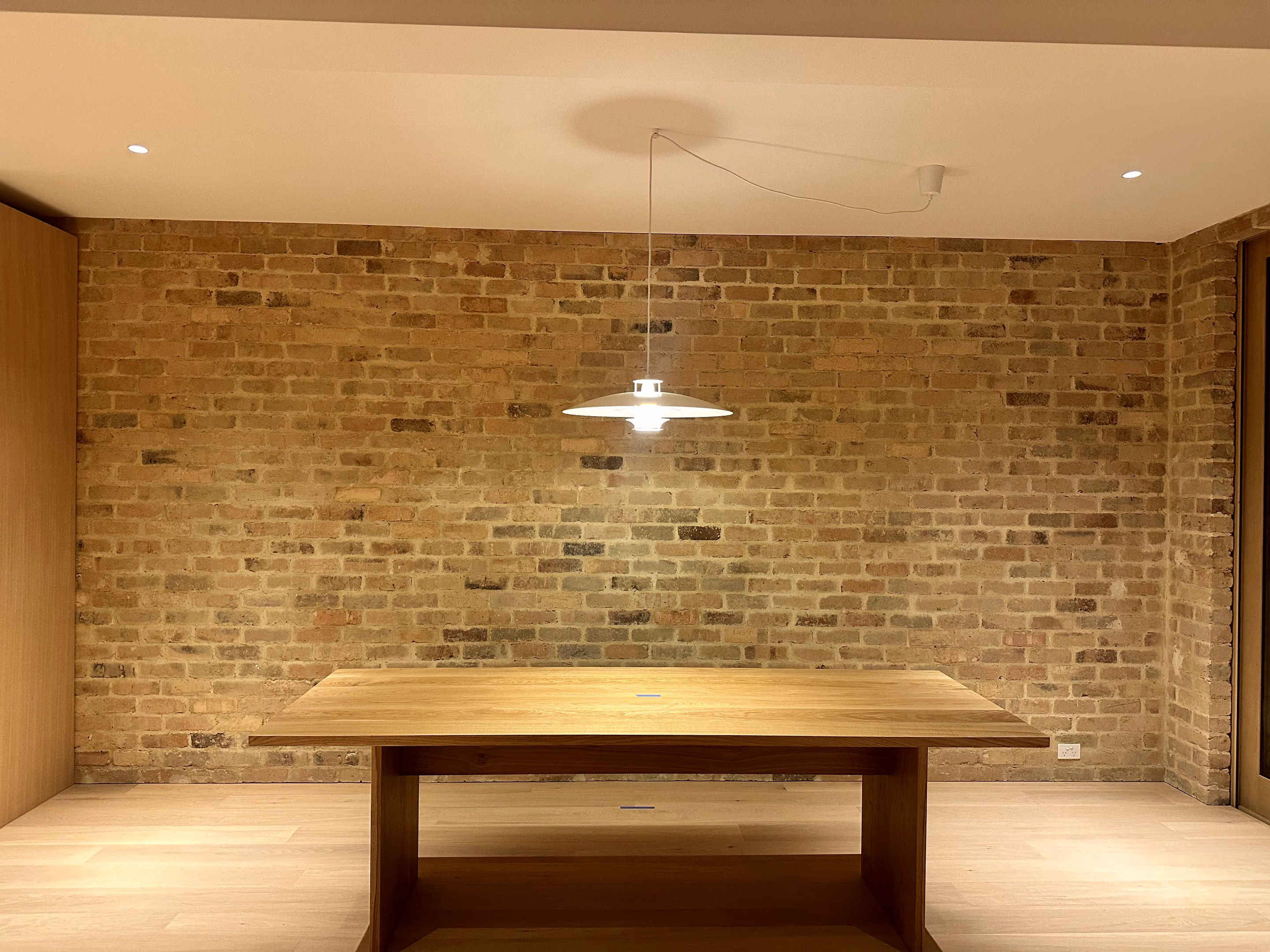 Pendant light over a timber dining table against an exposed brick wall