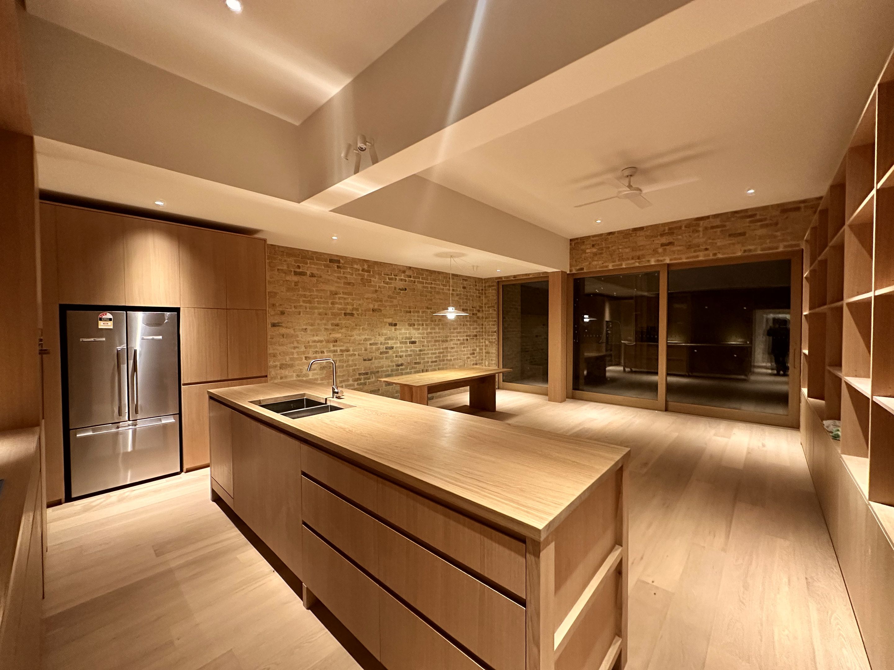 Kitchen island, refrigerator and open shelving beside a brick wall